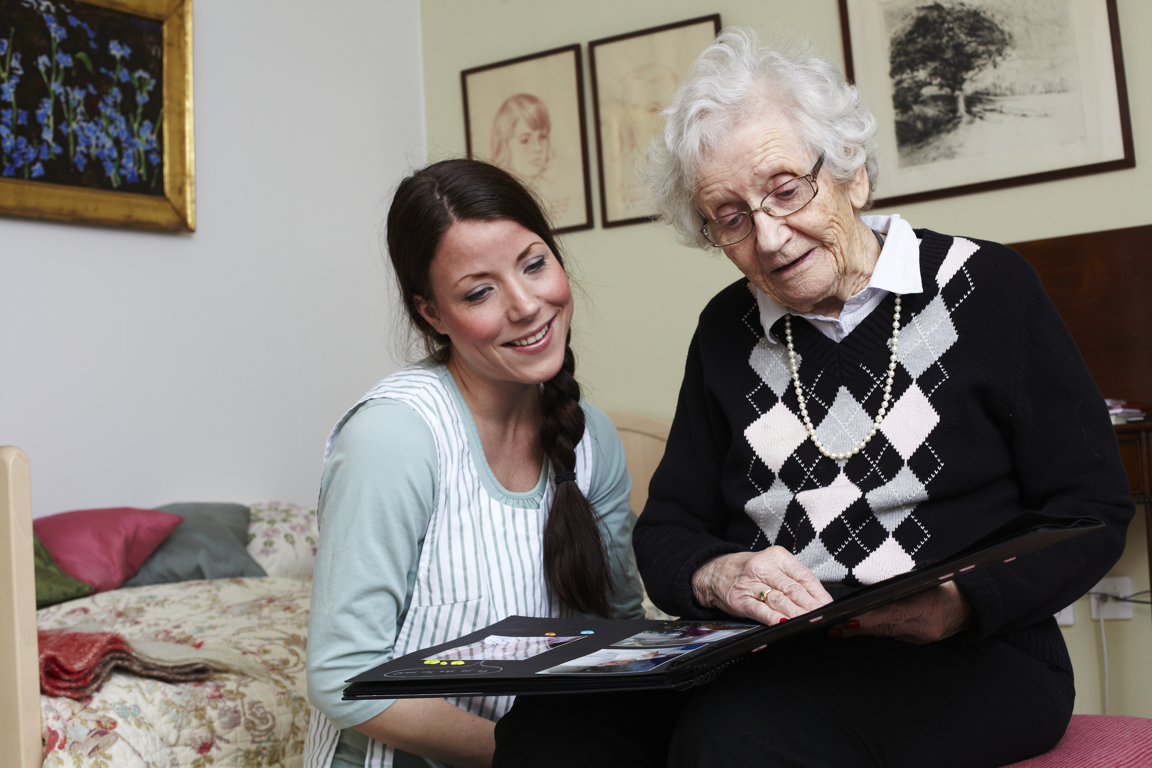 En gammal kvinna på vårdhem berättar om bilderna i ett fotoalbum för en kvinlig sköterska.