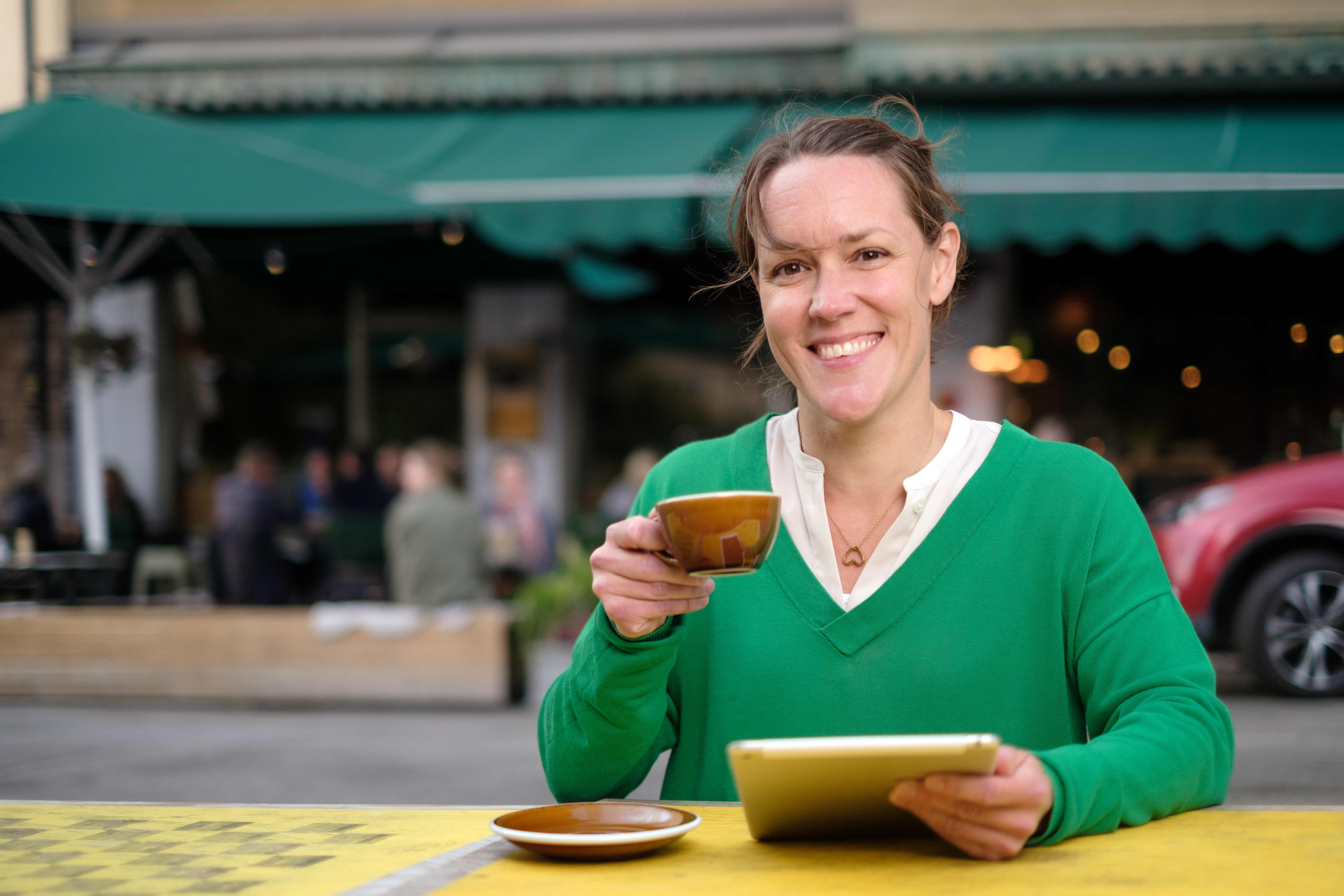 En kvinna sitter vid ett bord och håller i en kaffekopp och en surfplatta.