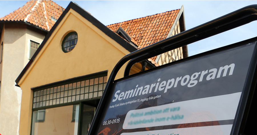 Skylt med seminarieprogram framför en husfasad i Almedalen.