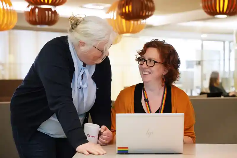 En kvinna och en kvinna med en kaffekopp tittar på en bärbar dator.