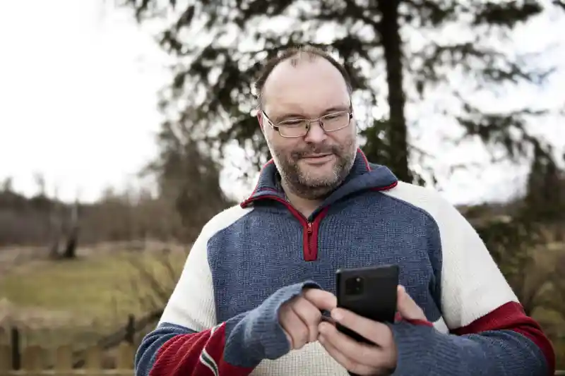 Man som står utomhus och använder sin mobiltelefon.