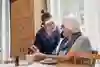 Äldre dam sitter med mobiltelefon och pratar med vårdpersonal.