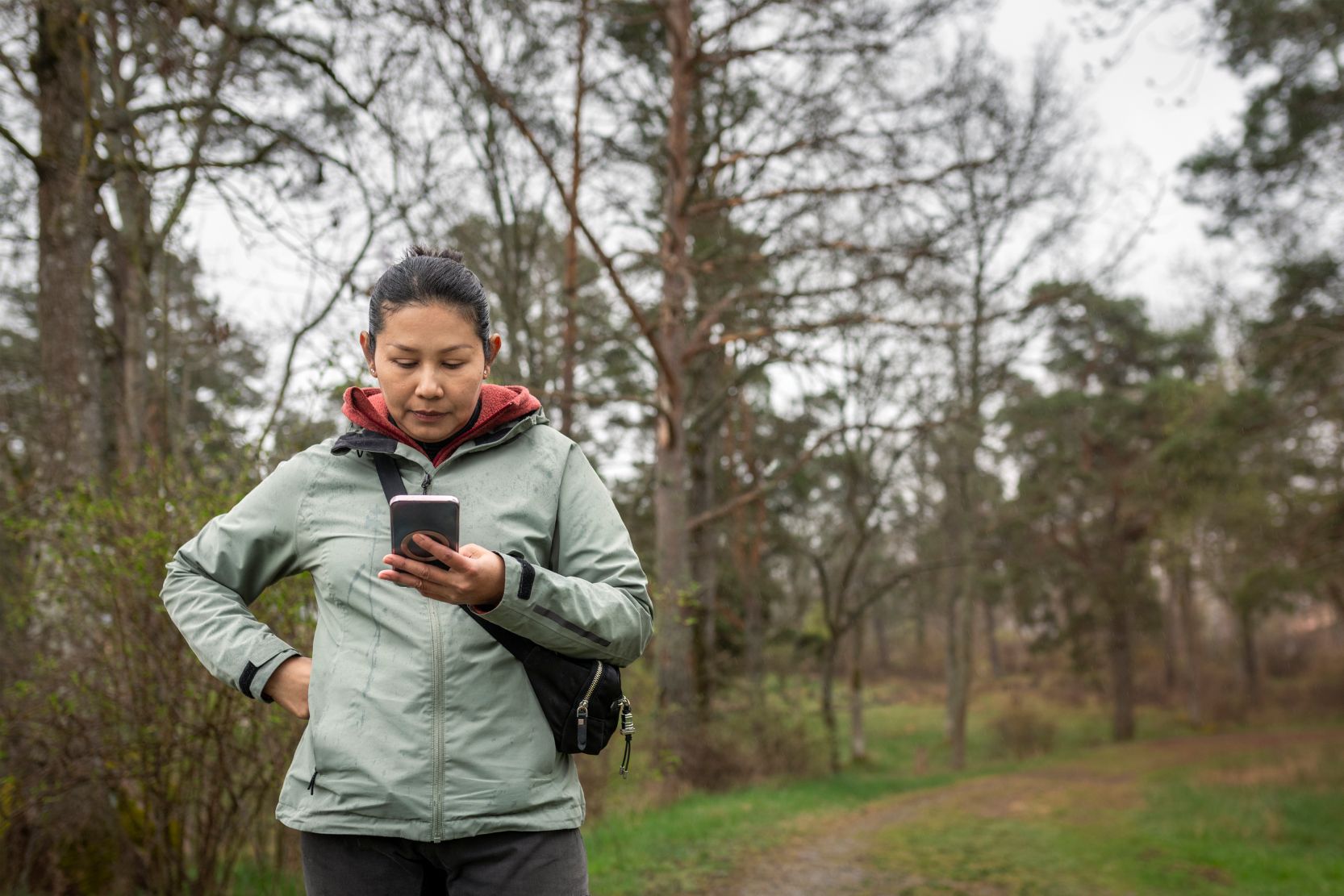 Person tittar på mobil i regn i naturen.