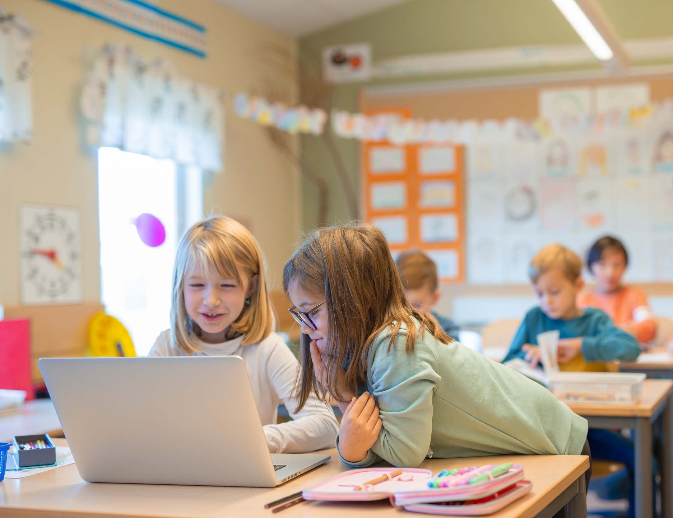 Två glada, unga skolflickor som tittar på en bärbar dator.