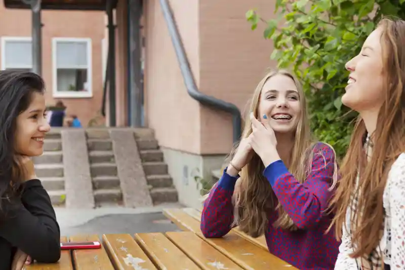 En grupp unga kvinnor sitter runt ett träbord på en skolgård.