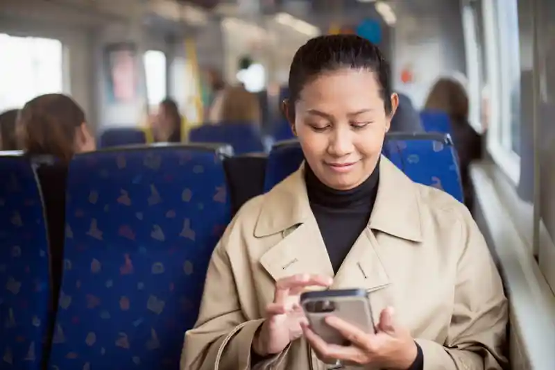 Bild på kvinna på tåg som kollar på sin telefon