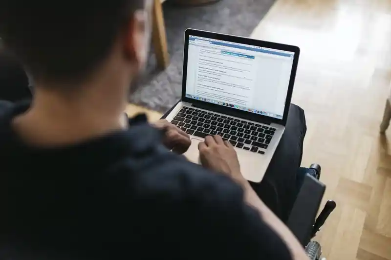 Person i rullstol med en bärbar dator i knät.