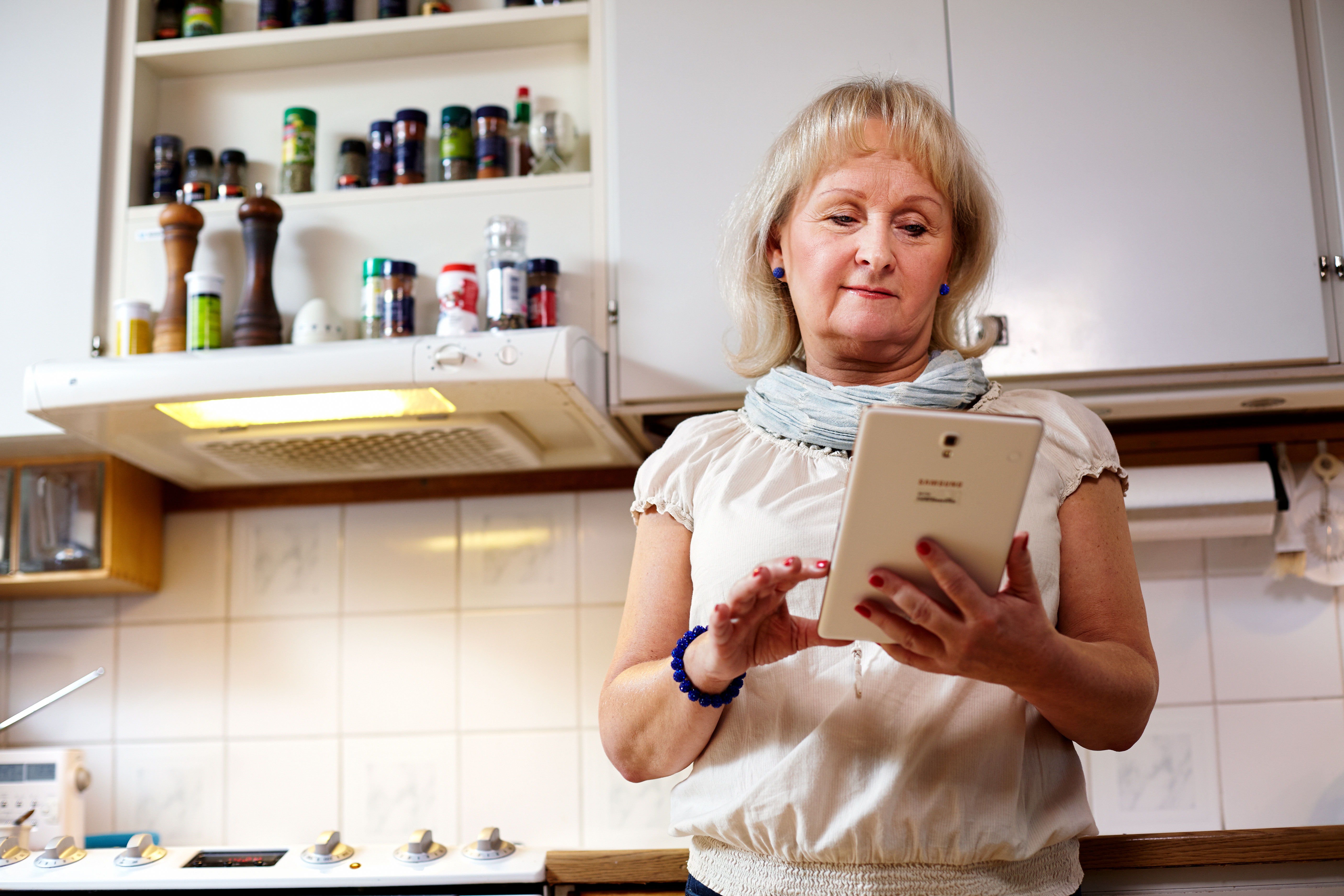 Äldre kvinna söker information på en läsplatta hemma i köket