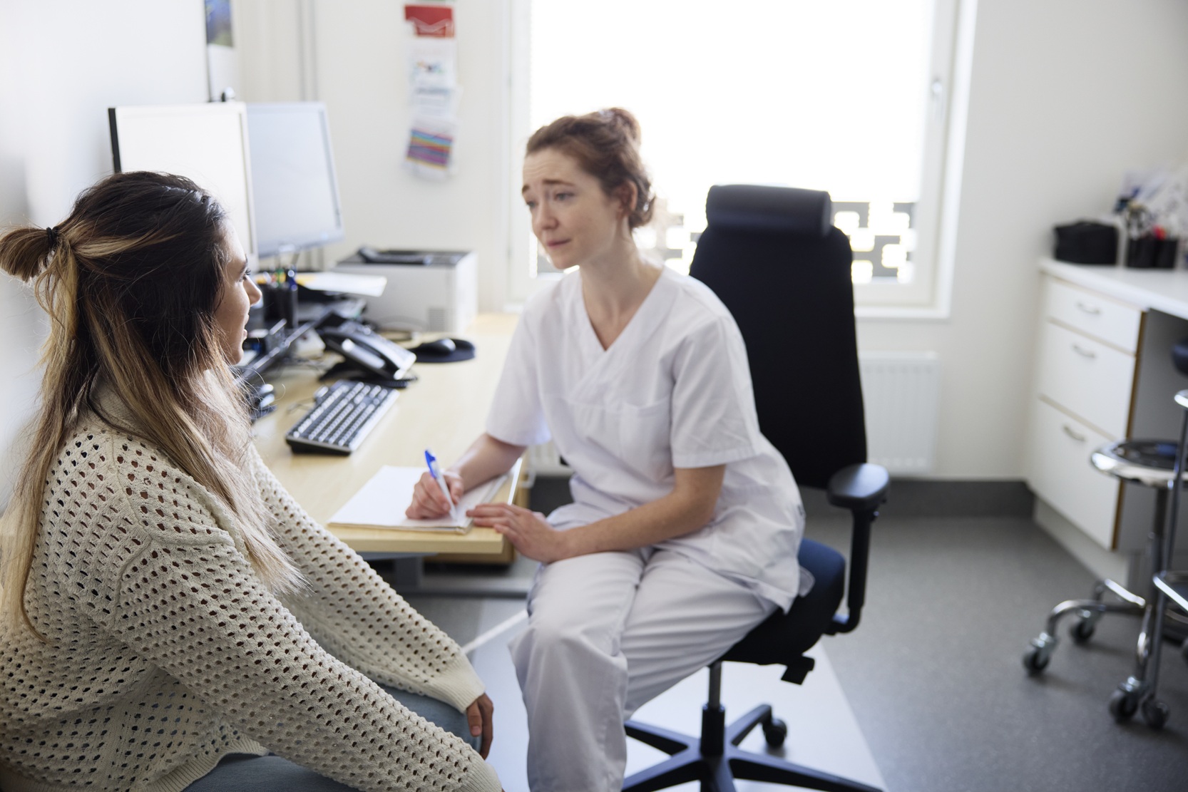 En kvinna sitter vid ett skrivbord och pratar med en annan kvinna.