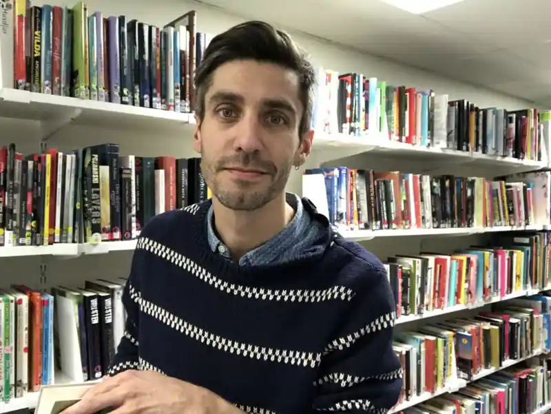 Leende man som står i ett sjukhusbibliotek och kollar in i kameran.